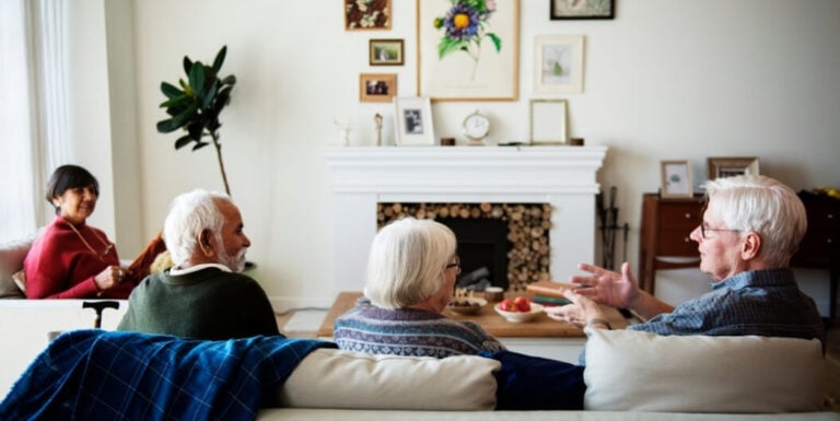 Elderly Friends Chatting by Fireplace with Family at Memory Care Facility